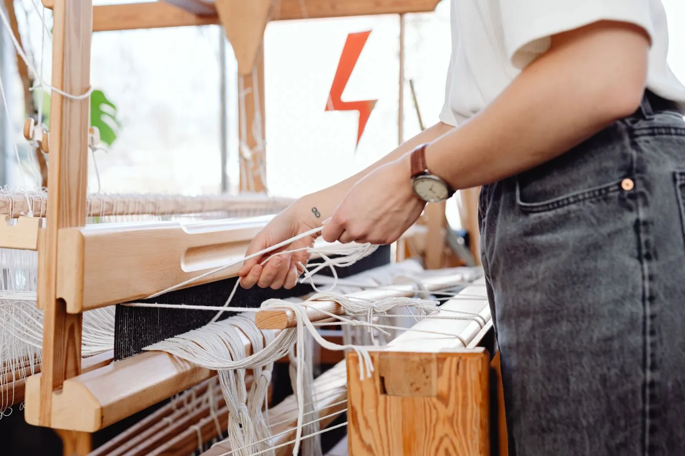 A weaver guiding threads through a wooden loom by hand